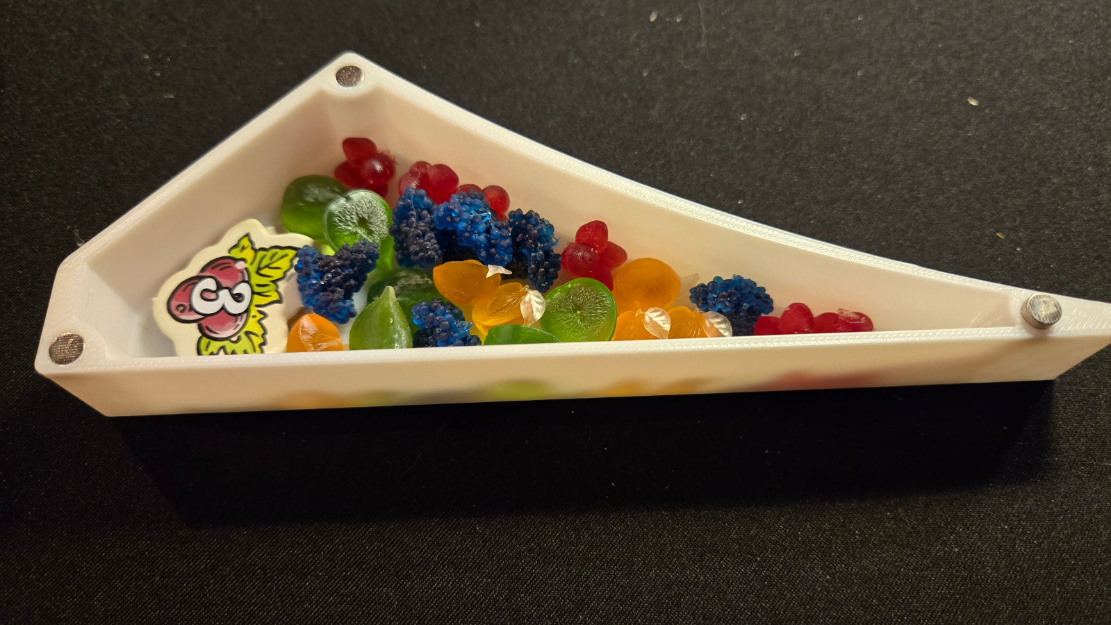 Triangular white dish with colorful gummy bears on a black background