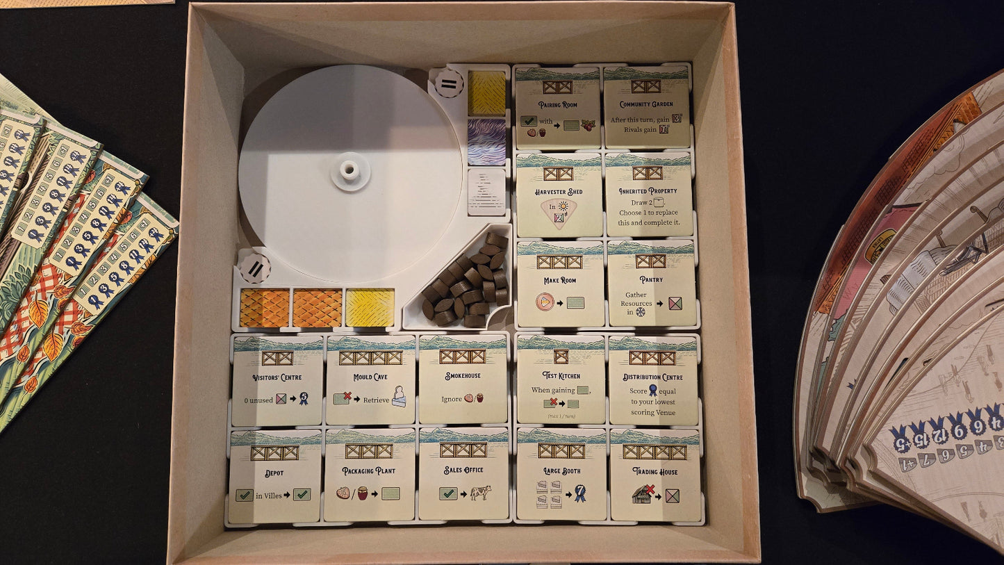 Collection of board game components including cards, dice, and boxes in a box on a dark surface.