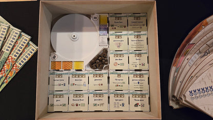 Collection of board game components including cards, dice, and boxes in a box on a dark surface.