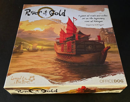 Board game box titled 'River of Gold' on a dark surface