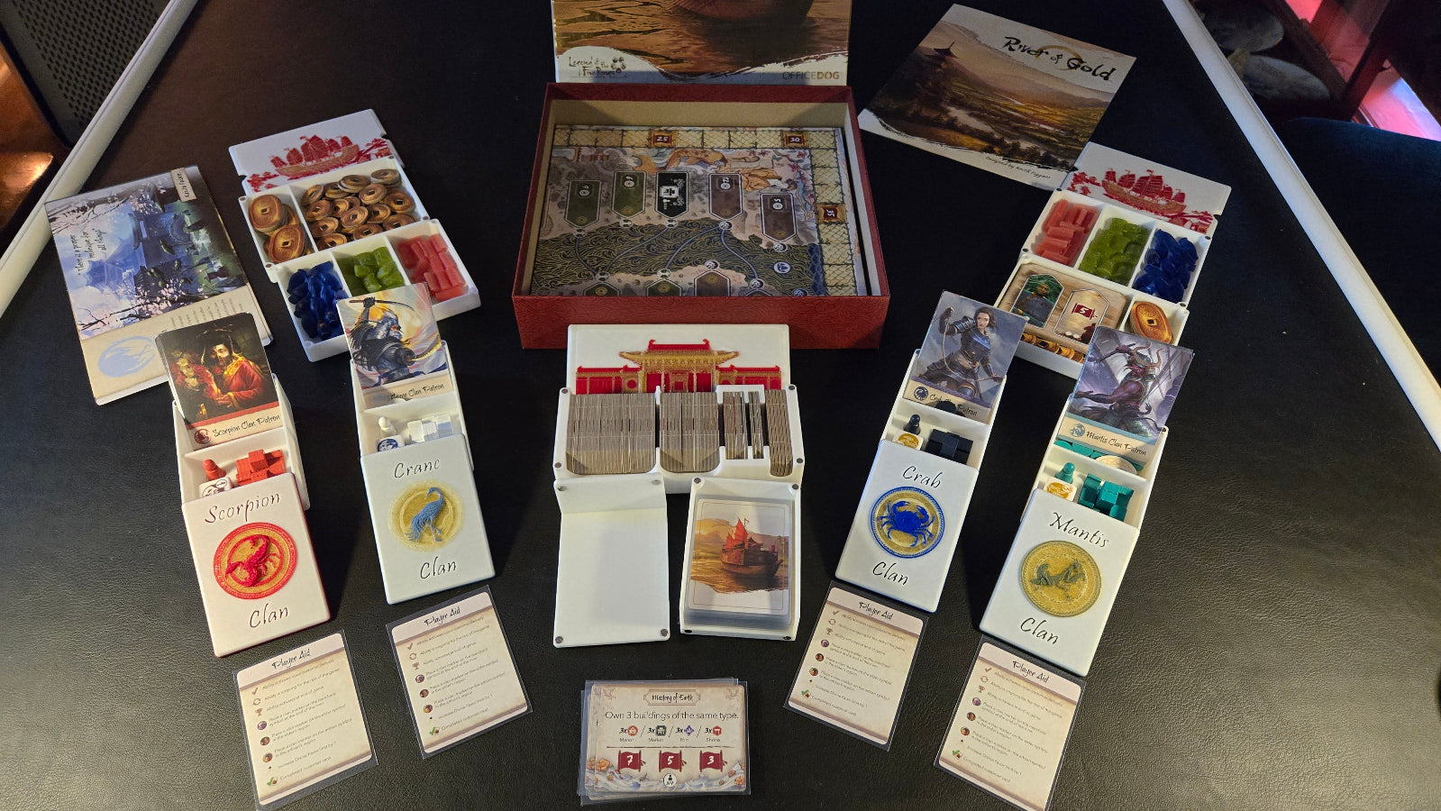 Board game components including cards and a box on a dark surface