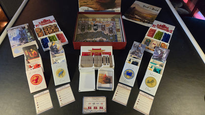 Board game components including cards and a box on a dark surface
