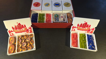 Colorful game pieces in a box with decorative lids on a dark surface