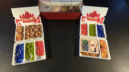 Board game components including cards and dice in a box on a dark surface