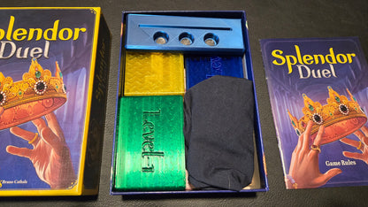 Splendor Duel board game components including box, cards, and rule book on a dark surface.