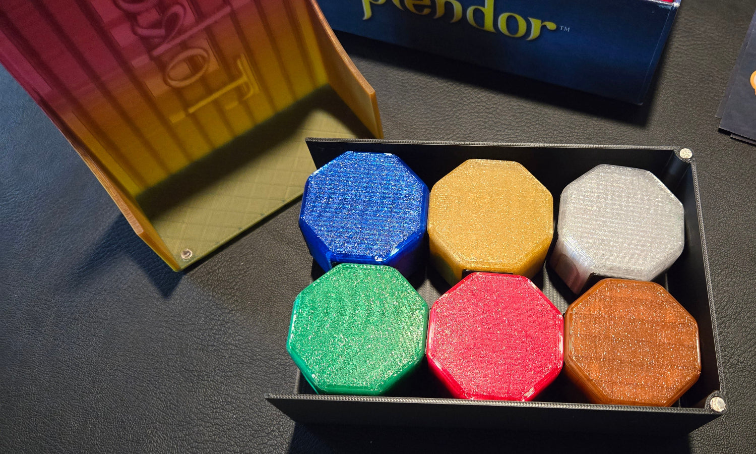 Set of colorful hexagonal game pieces in a box on a dark surface with 'Prendor' branding.