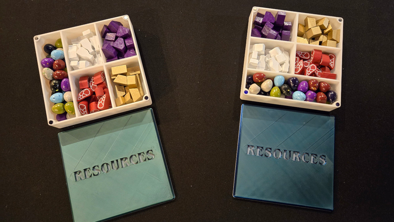 Two trays with compartments filled with colorful items and 'RESOURCES' labels on a dark surface.
