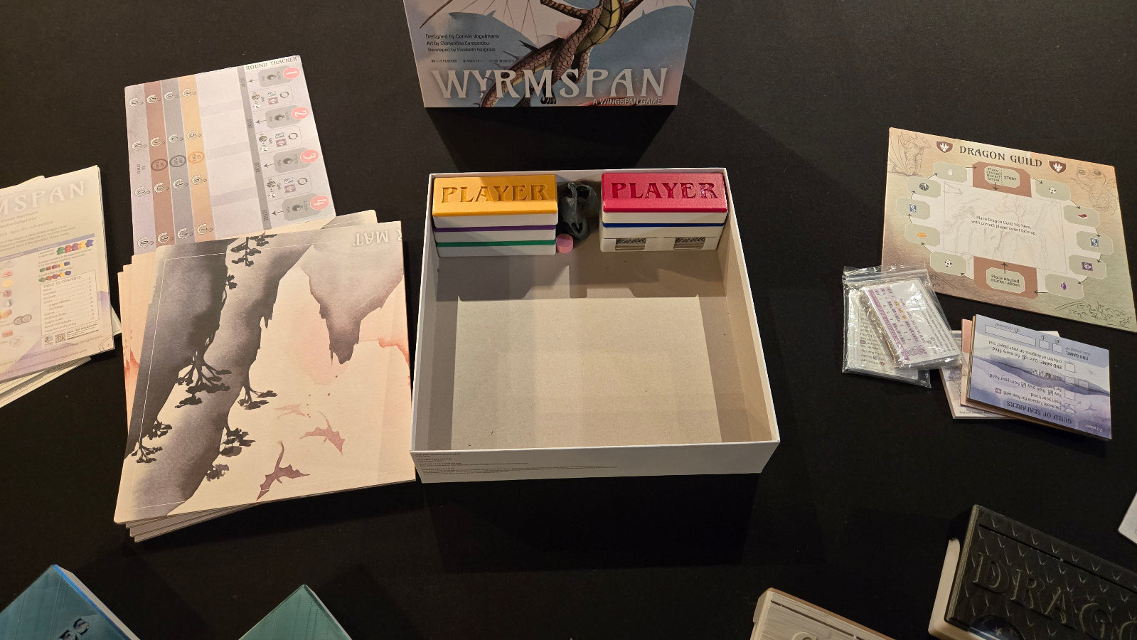 Collection of game components including cards and a box on a dark surface