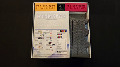 Game components including player sheets and a dragon model in a box on a black background